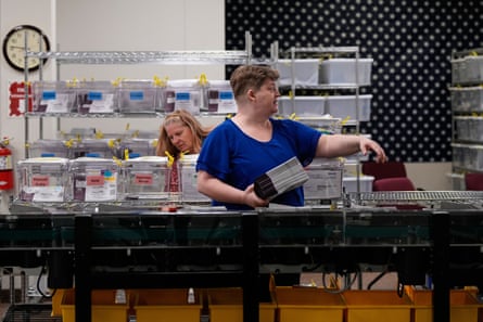 Two women at tables with shelves and plastic contaienrs.