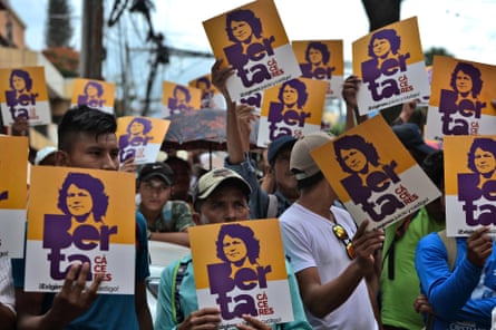 A group of people hold up yellow and white signs with purple writing that reads ‘Berta!’ and a purple portrait of a woman.