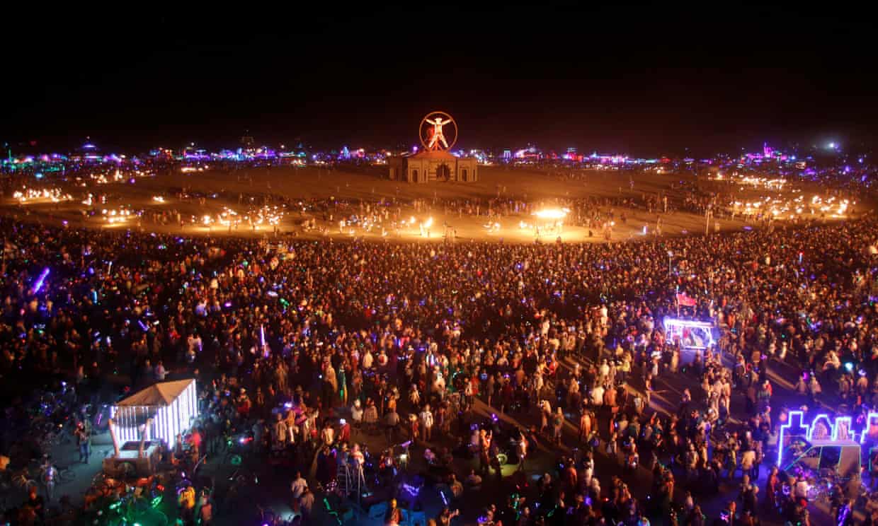 A birds eye view of a desert festival filled with people and fire with a burning wood man-like figure in the middle.