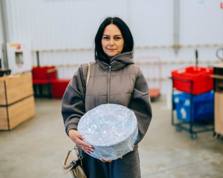 A woman with dark hair stands in a warehouse holding a round package