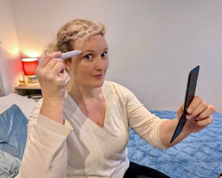 The writer uses an eyebrow and face epilator while looking in a handheld mirror.