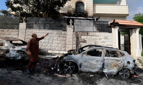 A man beside burnt cars points at the damage in his West Bank house in Jit village, a day after the attack by Jewish settlers