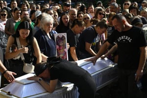 A weeping woman rests her forehead on a coffin surrounded by other mourners