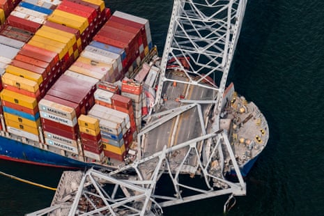 a destroyed metal bridge rests on a large boat with many different colored shipping containers stacked up high