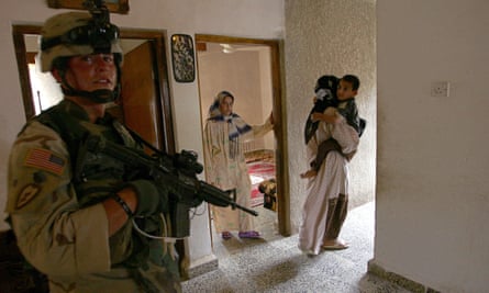 Iraqi women stand in their living room close to a US soldier while their home is searched.