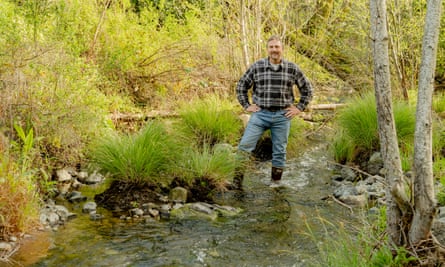 A man in checked shirt and jeans stands in a stream