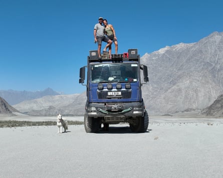 Bobby Bolton and Claire Deleval standing on top of the truck in a desert with a dog sitting below