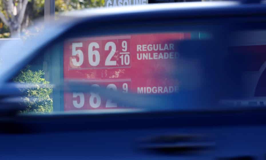 A blue car drives past a sign advertising gas prices at $5.62 a gallon.