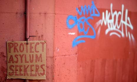 A cardboard placard saying "protect asylum seekers" on a wall with graffiti. sign  The asylum seeker’s lawyer said she experienced ‘dehumanising treatment’ but added that the case was ‘more about a system that breeds such treatment … an outcome of the government’s hostile environment policy’.
