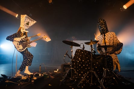 A guitarist and drummer with black-and-white polka dot masks and costumes