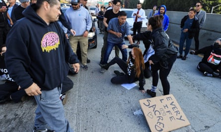 It appears that a woman has been pushed to the ground, alongside a cardboard sign that says, ‘Every life is sacred.’