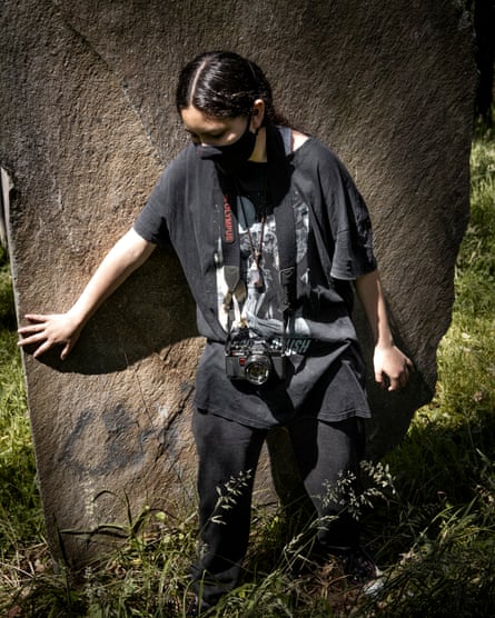 A teenage girl stands next to a tree with a camera around her neck