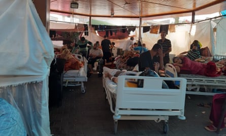 People sit on hospital beds under what looks to a wooden structure with curtains hung around for privacy