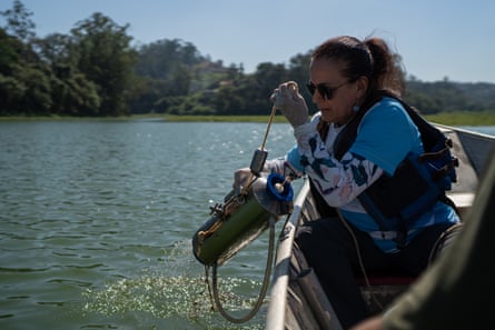 A woman in a small boat collects water using a container from a reservoir.