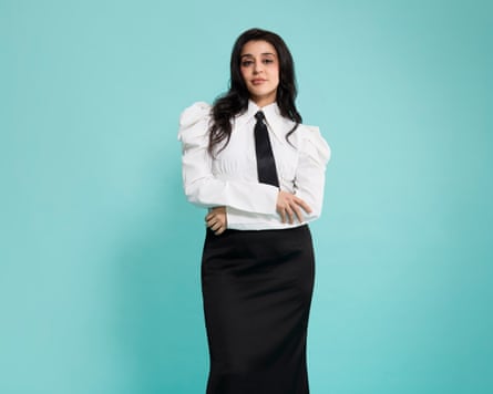 Portrait of Tareena Shakil against a blue/green backdrop. She is wearing a white shirt, black tie and black skirt