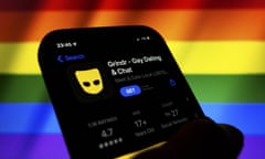 App icon of Grindr displayed in the App Store on a phone backdropped by cropped waving flag of the LGBT 