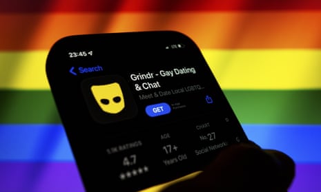 App icon of Grindr displayed in the App Store on a phone backdropped by cropped waving flag of the LGBT