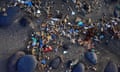 Small plastic parts and microplastics of varying colors in the sand of a beach surrounded by rocks