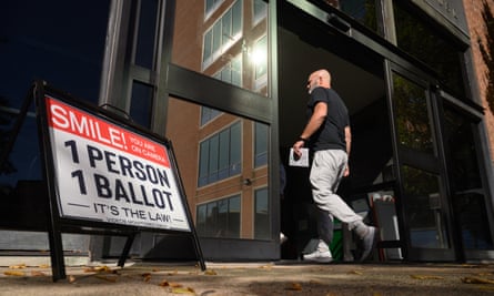A man enters the Bucks County administration building holding a ballot paper in Doylestown, Pennsylvania. He is going past a sign that reads: Smile! You are on camera. One person, one ballot. It’s the law