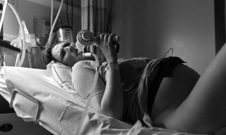 Pregnant woman in pain during labour taking gas and air mixture to relief pain