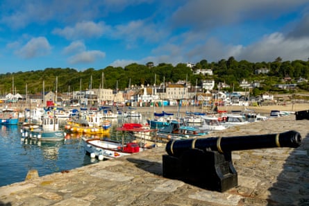 A jetty built from honey-coloured rock with a cannon on top and colourful boats in the harbour behind.
