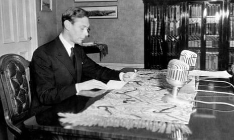 King George VI sits at a desk in front of two large microphones