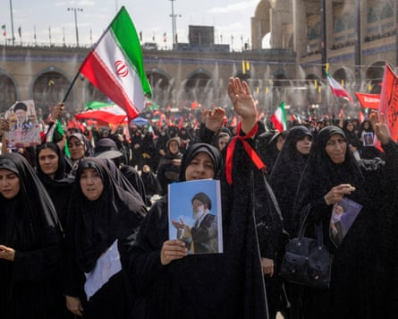 Women in black chadors hold up photos of Ali Khamenei and wave flags