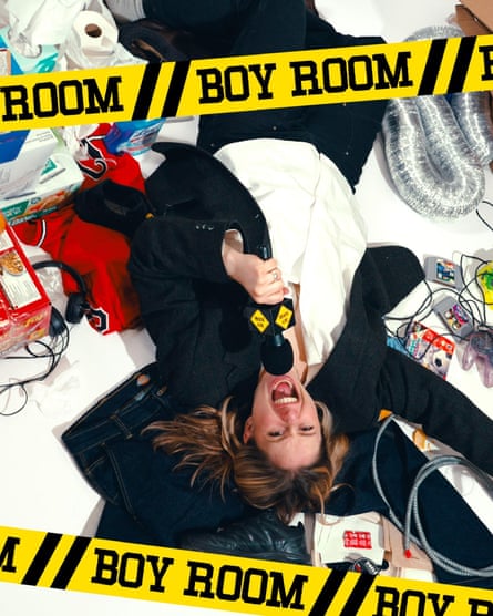 coster yells into mic as she lies in a mess, in a promo pic with an overlaid illustration of caution tape that says ‘boy room’