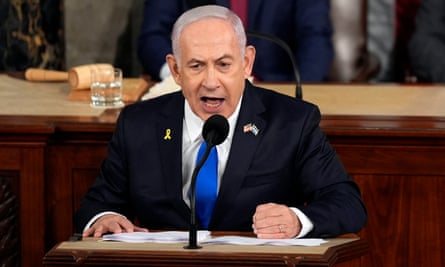 Benjamin Netanyahu sitting at a table with a microphone in front of him