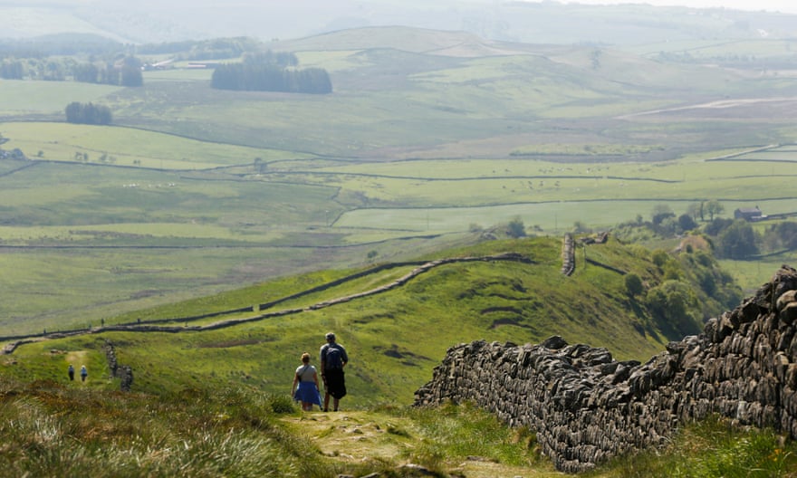 Walkers alongside a section of Hadrian’s Wall with a magnificent view of rolling countryside ahead.
