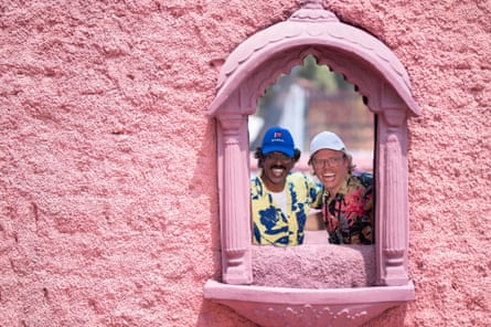 Romesh Ranganathan and Rob Beckett in Mumbai looking through an ornate pink window frame set into a pink wall .