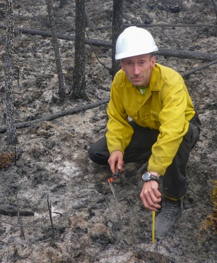 A man in a hard hat crouches on scorched earth. 