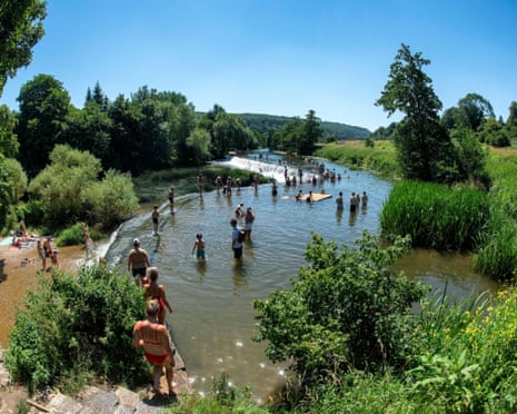 People in bathing suits descending down steps to join others standing in river surrounded by greenery.
