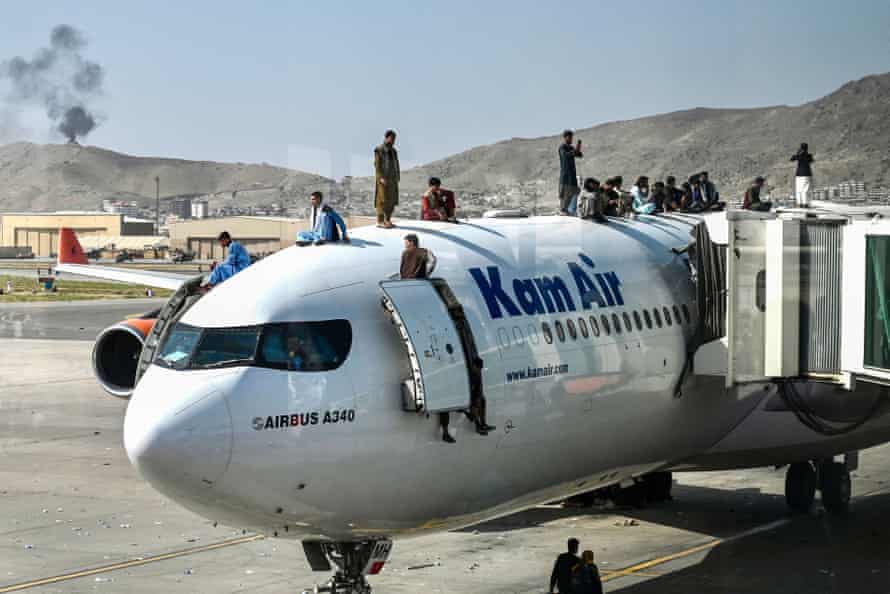 Afghan people climb atop a plane as they wait at the airport in Kabul on August 16, 2021, after a stunningly swift end to Afghanistan’s 20-year war, as thousands of people mobbed the city’s airport trying to flee the group’s feared hardline brand of Islamist rule.