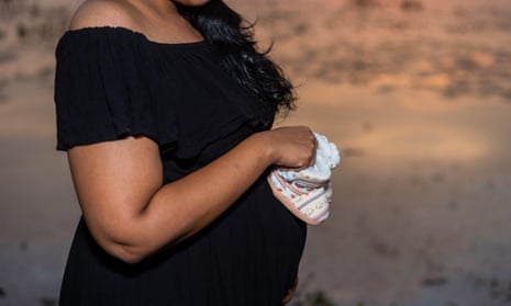 Pregnant woman in black gown holding baby boots 