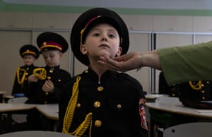 A boy in cadet uniform sits at a desk as someone holds up his chin