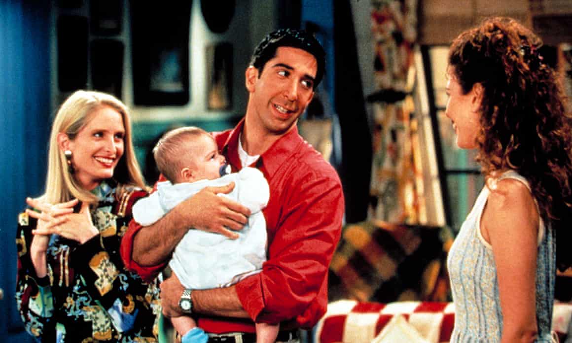 Jane Sibbett smiles as David Schwimmer holds a baby, while Jessica Hecht looks on
