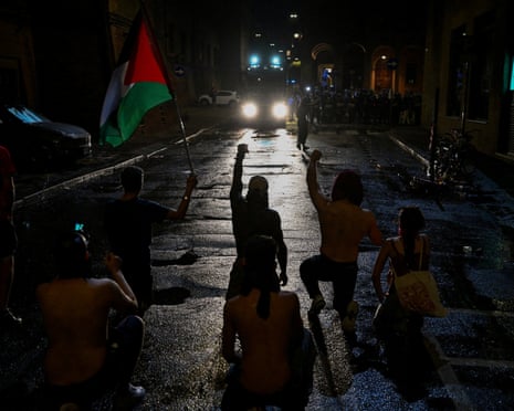 Protesters kneel and raise their fists while facing a police line during a demonstration following the death of Abderrahim Fakir in Bologna, Italy.