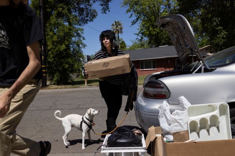 woman takes box out of car trunk while her dog watches