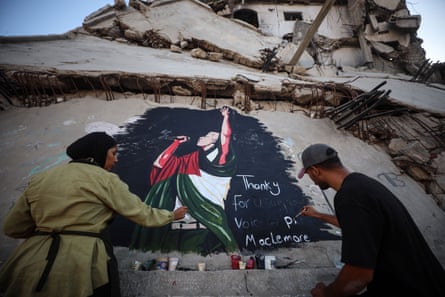 A woman in a beige overcoat and a man dressed in black paint a mural of a singer draped in red, green and white