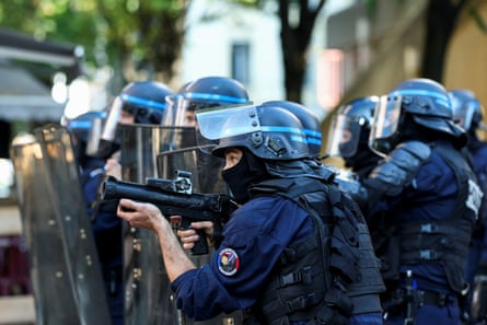 A French police officer aims a crowd-control weapon surrounded by colleagues.