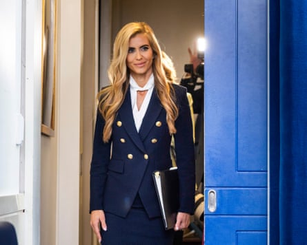 Katie Zacharia, White House press secretary, walks through a doorway holding a black binder