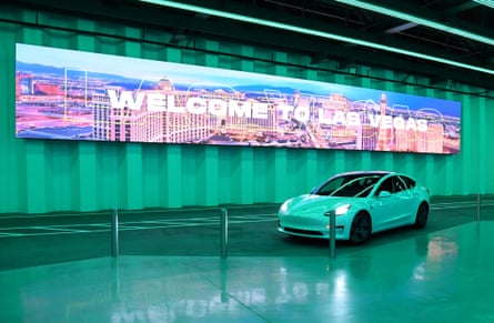 A white Tesla is shown in a dark underground area with green lighting.