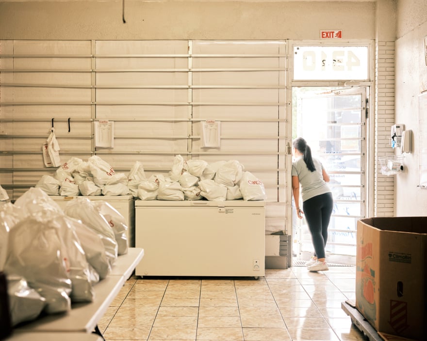 A woman leans on the store's eaves.  The space is filled with freezer boxes with food bags piled on top.