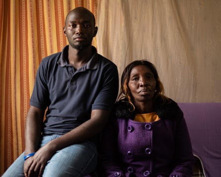 Philip Kuria and Jacinta Kabiru; he sits on the arm of a purple sofa above his mother. There is a yellow and rust-brown striped curtain behind them; he wears a dark blue polo shirt and she wears a purple coat.