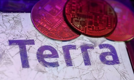 Terra logo displayed on a phone screen is seen through a broken glass with representation of cryptocurrency 