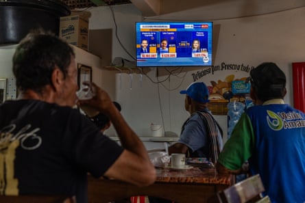 Men sit drinking coffee and beer and looking at a wall-mounted TV.