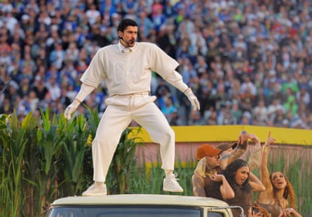 Bad Bunny stands atop a van roof in a cream football uniform during the halftime show