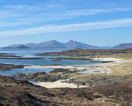 White sand beaches by a rocky shoreline with mountains in the distance