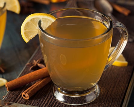 A glass mug of hot toddy with a lemon slice on the rim, beside cinnamon sticks